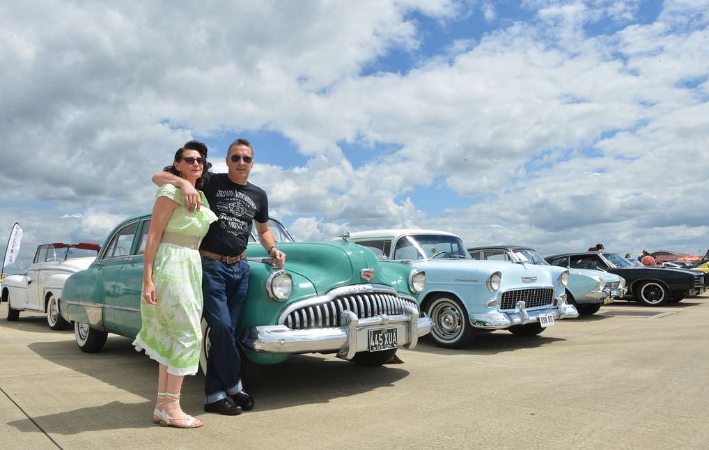 A man and woman standing next to classic cars.